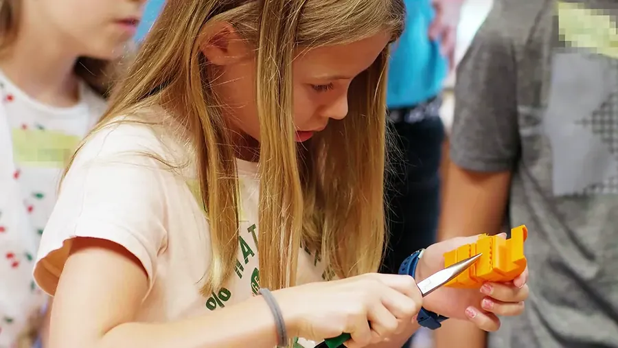 Eine Schülerin entgratet ein orangefarbenes 3D-gedrucktes Teil