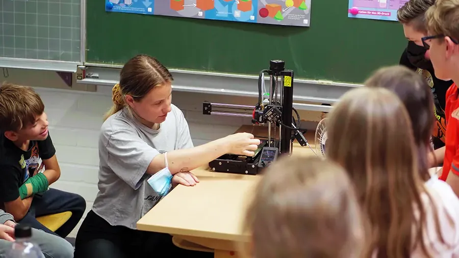 Eine Lehrerin erklärt einer Schülergruppe den 3D-Drucker