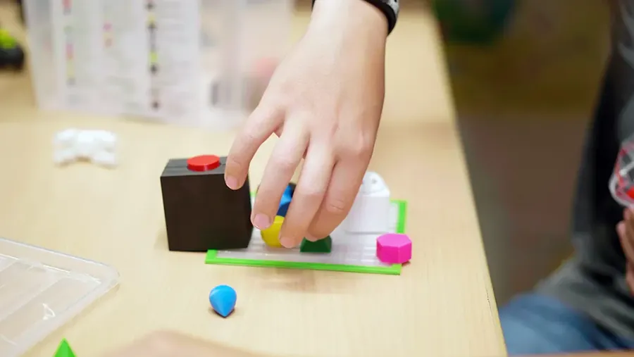 Eine Kinderhand setzt 3D-gedruckte Grundformen auf eine Platte