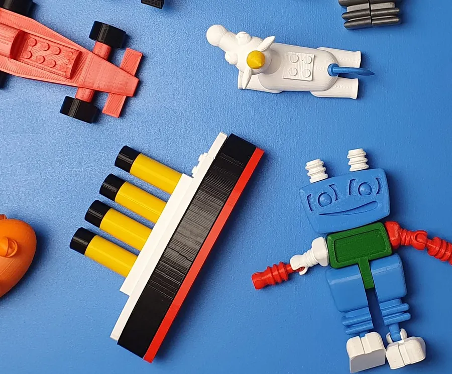 3D-gedruckte Modelle auf blauem Tisch: ein Rennwagen, ein Einhorn, ein Schiff und ein blauer Tim-Tinker-Roboter