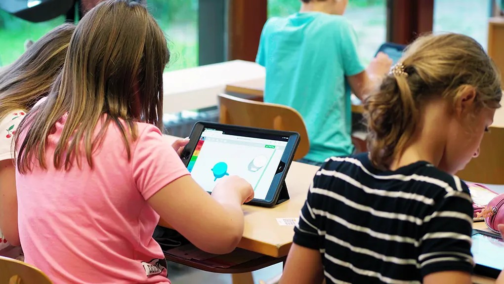 Eine Schülerin baut am Tablet ein Modell, daneben arbeiten weitere Kinder