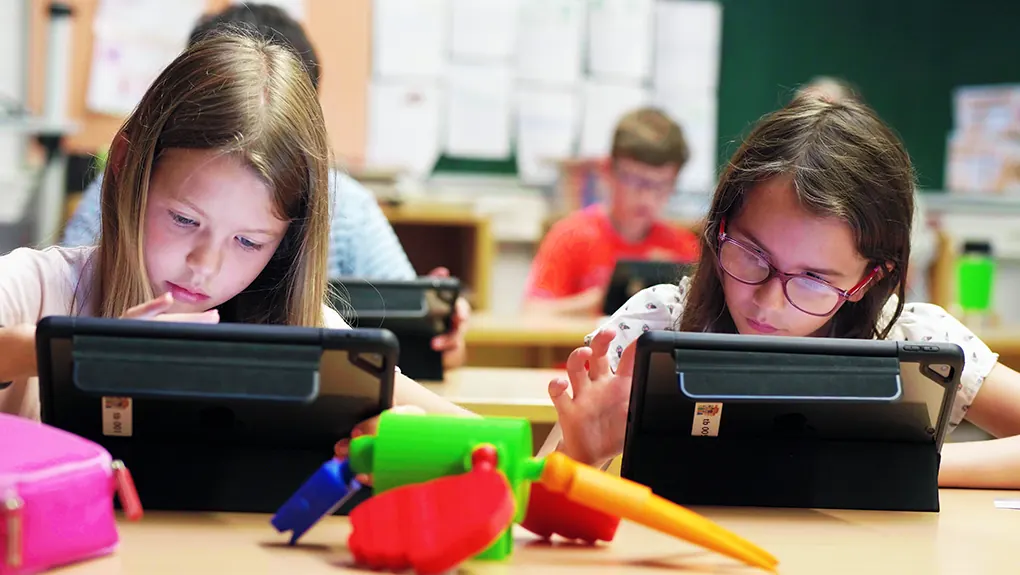 Zwei Schülerinnen arbeiten an Tablets, vor ihnen liegen 3D-gedruckte Teile